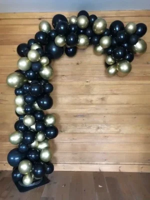 Black and gold balloons arranged in an arch against a wooden wall.