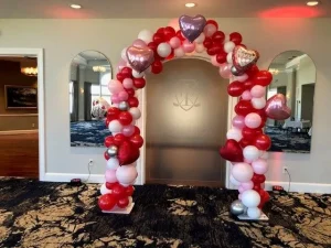 Red, pink, and white balloon arch with heart-shaped balloons stands in front of frosted glass double doors.