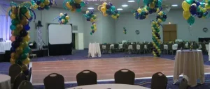 Balloon-decorated banquet hall with tables and chairs arranged around an empty dance floor.