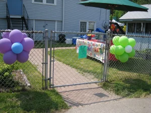 A fenced yard decorated with flower-shaped balloons and a table covered with a colorful tablecloth.